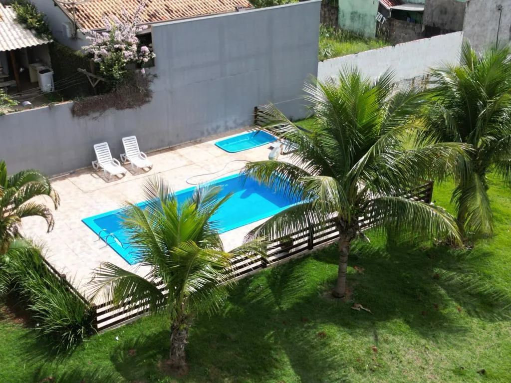 Vista aérea da piscina do Espaço ToaToa: piscina principal azul, piscina infantil, deck com espreguiçadeiras, cerca de madeira e coqueiros