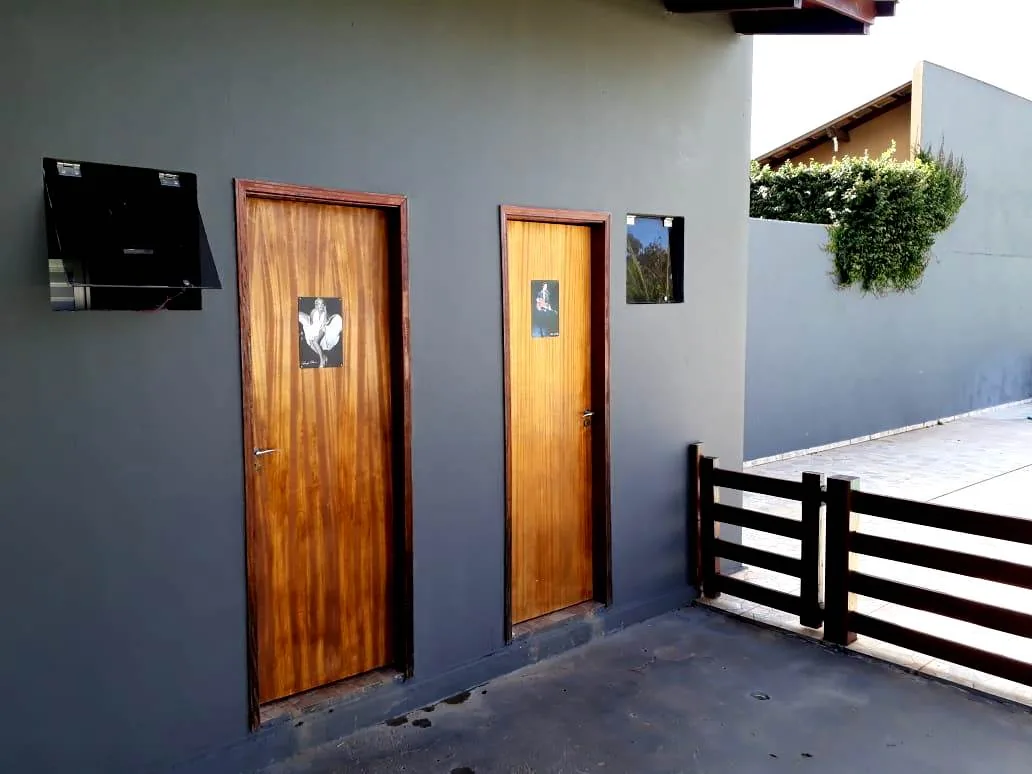 Dois banheiros com portas de madeira na parede cinza da área coberta, ao lado da cerca da piscina