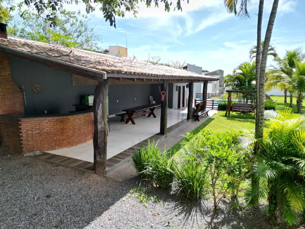 Lateral da varanda coberta com jardim, cascalho, coqueiros e o balanço de madeira ao fundo
