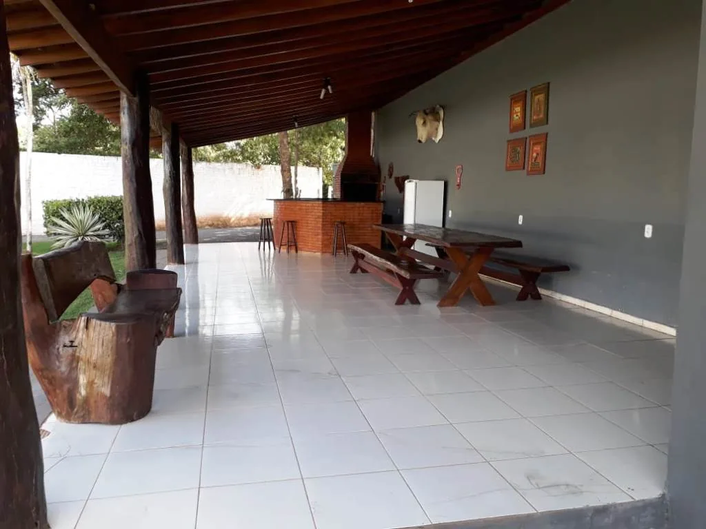 Varanda coberta com piso branco, telhado de madeira, mesa rústica com bancos e banco de tronco